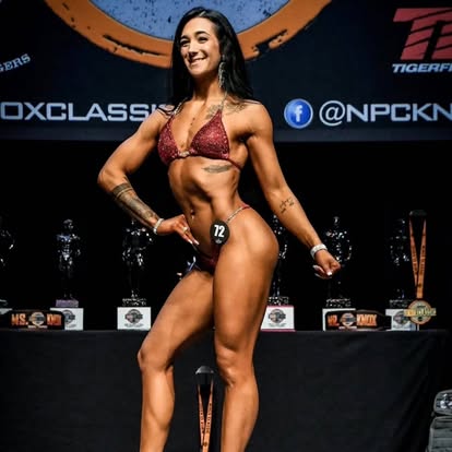 Legion athlete posing on an NPC stage in front of trophies